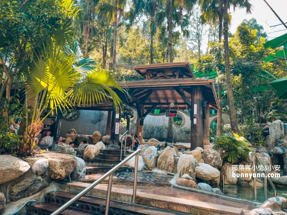 Tranh dán tường phong cảnh khu suối nước nóng với cổng gỗ, hồ đá và rừng nhiệt đới xanh mát