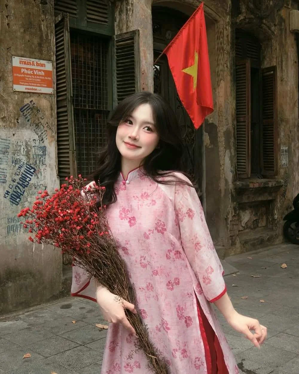 Gái đẹp Việt Nam mặc áo dài hồng cầm hoa khô trước cờ Việt Nam