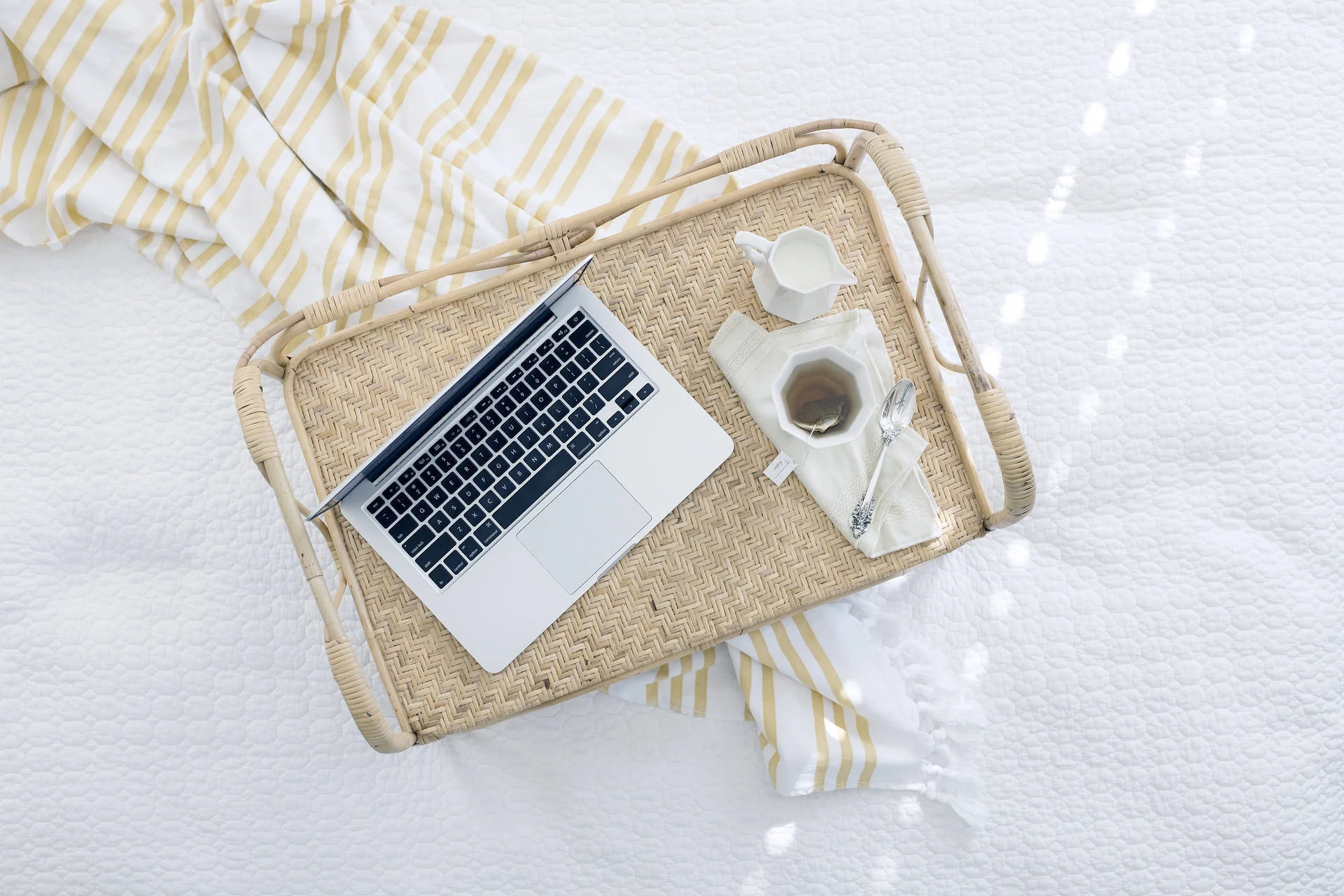 Laptop và tách cà phê trên khay mây đặt trên giường sáng màu